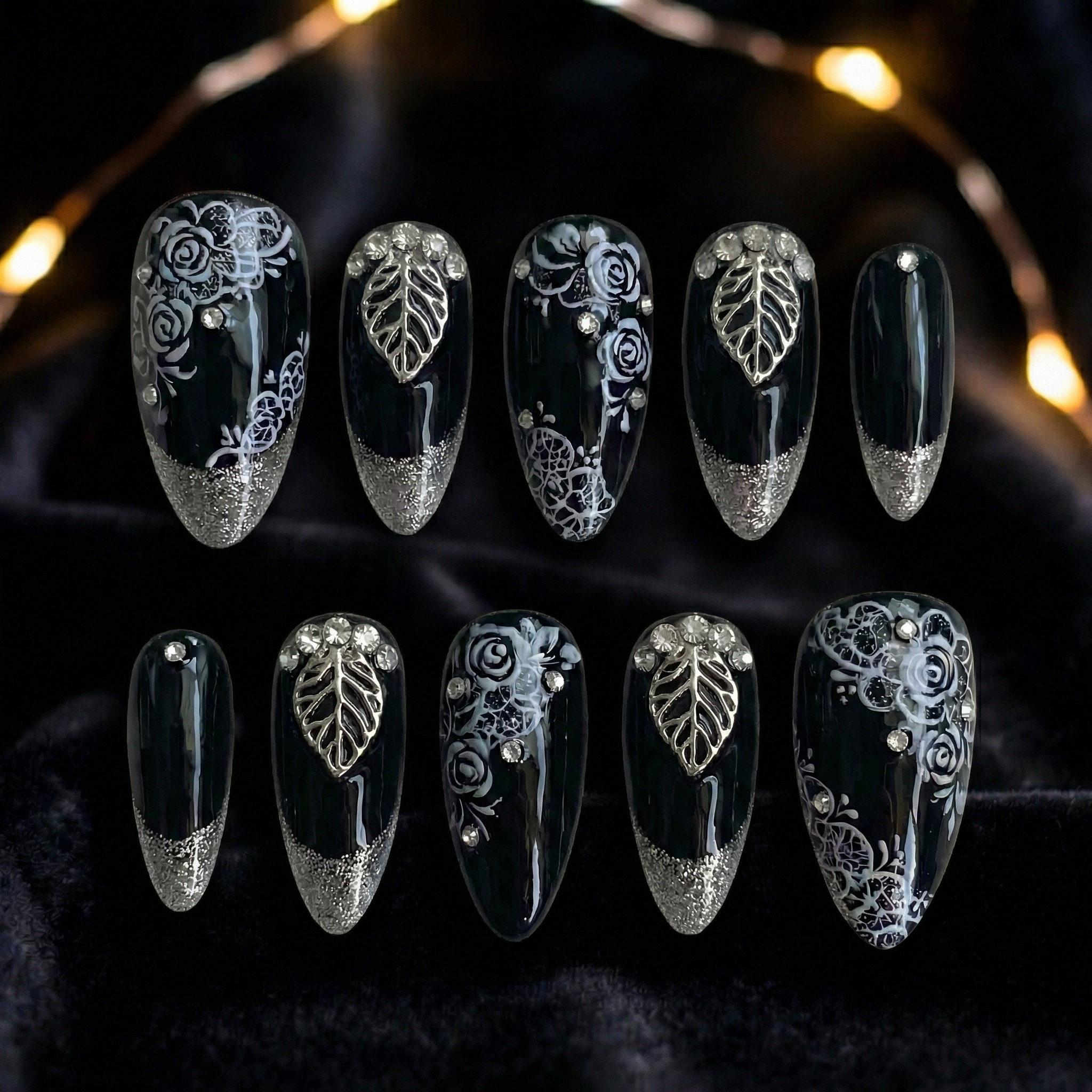 Black press-on nail with silver leaf design flat lay